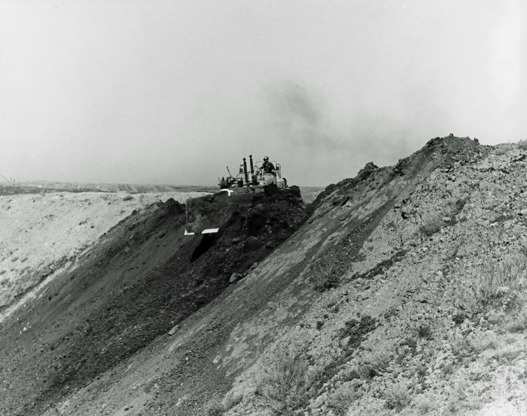 Bulldozer on a hillside, constructing, with smoke and a vast landscape in the background.