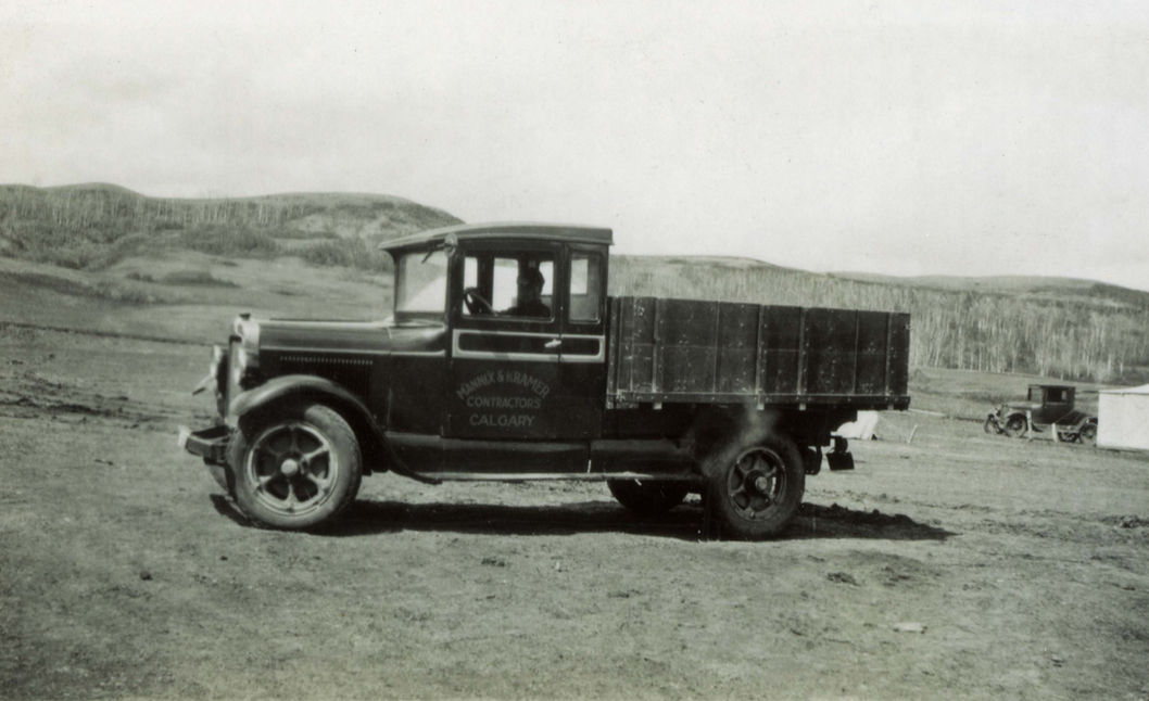 Vintage black truck on a dirt road with text and hillside background.