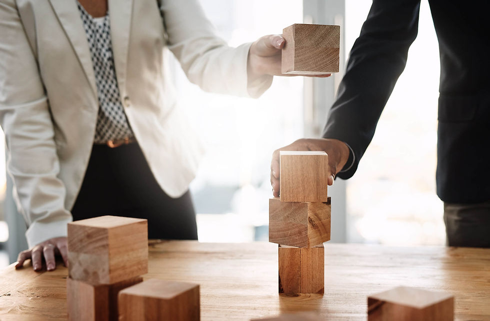 Two professionals building tower with wooden blocks on a wooden table at the Coril Holdings office in Calgary