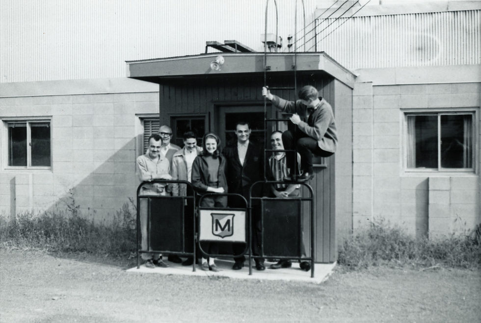 Group poses in front of building with sign, man climbing ladder, vintage photo.