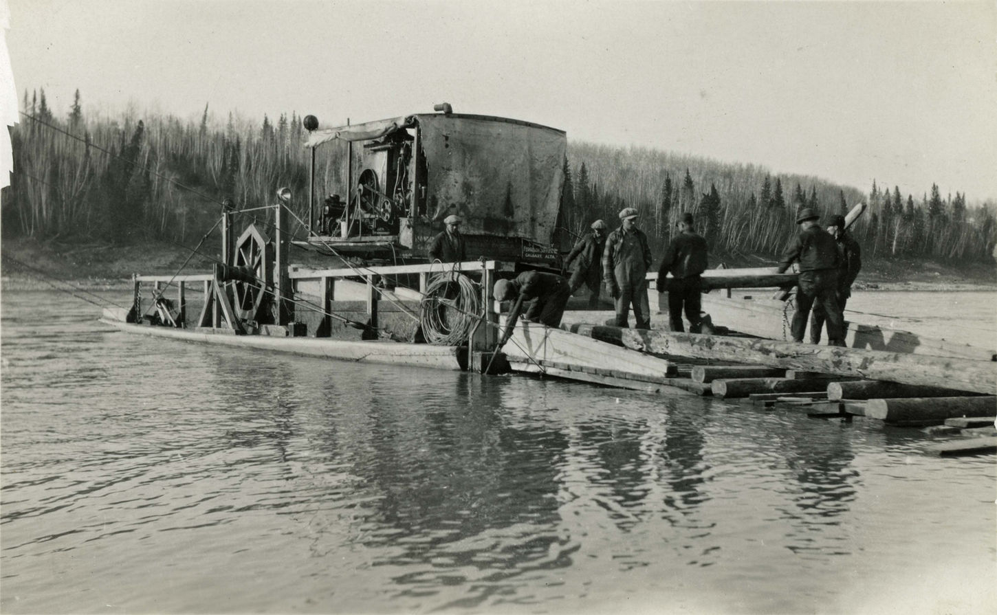 Men loading logs onto a raft in river near trees, Legacy, vintage photo.